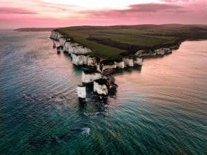 Aerial view of Studland rocks. White cliffs emerge from a blue sea against a pink sunset sky.