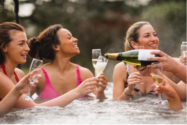 Group of women drink champagne and laugh in a hot tub.